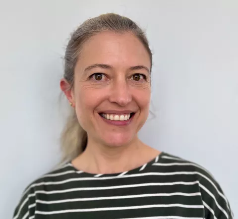 A smiling white woman with a long ponytail, wearing a black and white striped shirt.