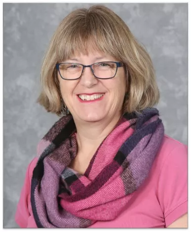 A smiling white woman with a pink t-shirt and pink and purple scarf.